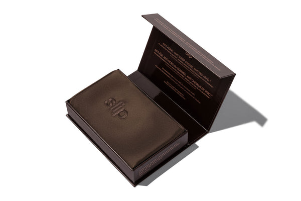 A dark chocolate brown silk pillowcase box shown open on a white background, with the brand name 'slip' embroidered on the pillowcase.