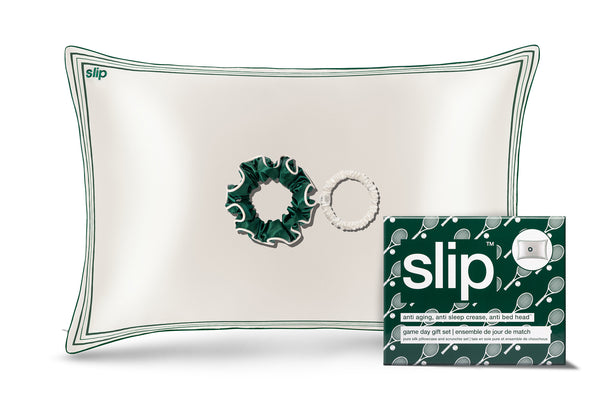 A white silk pillow with green decorative trim and piping, a green silk large scrunchie and a skinny white scrunchie with slip packaging on a white background