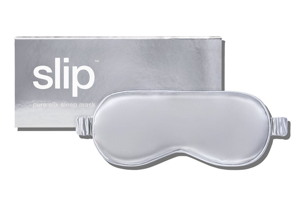 A silver slip silk sleep mask in front of branded packaging on a white background.