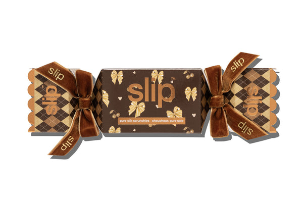 Slip scrunchies in a cracker-style box with brown and beige argyle patterns, ribbon bows, and the brand name 'slip' printed on the ribbon and front.