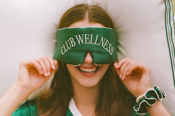 Person wearing a green 'Club Wellness' block out sleep mask with a white background